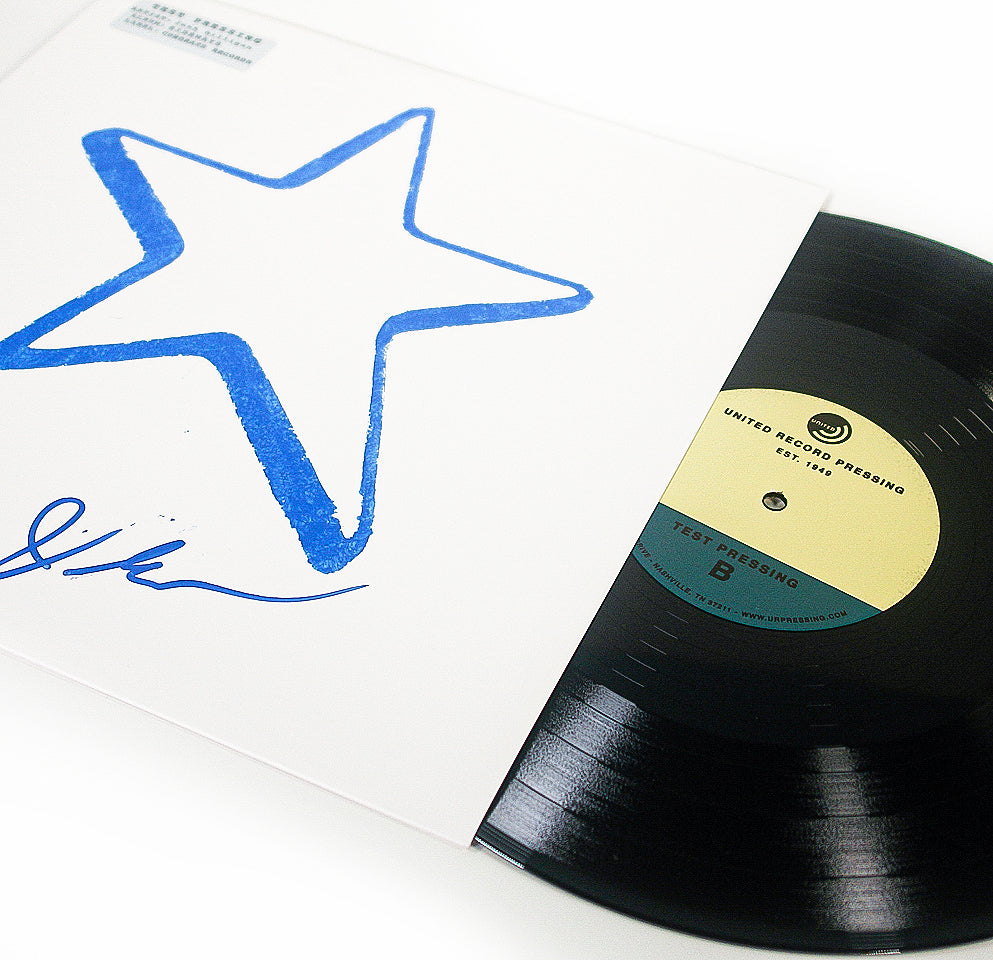A vinyl record partially slides out of a white sleeve featuring a large blue star and a signature. The record has a beige label marked Test Pressing, hinting at exclusive tracks like “Summers Ending” gracing its unique track listing.