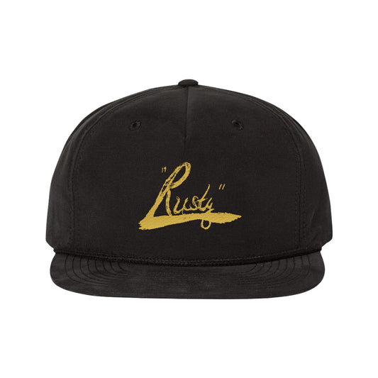 A black 5-panel hat by Rusty Williams with Rusty in gold script on the front, featuring an adjustable snapback closure for a comfortable, classic fit.
