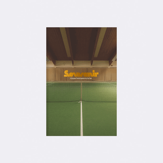 A green indoor tennis court with a net sits beneath exposed wooden beams. Above the court, Souvenir (the brand name) appears in yellow, with smaller white text below, evoking a Racquet Magazine feel.