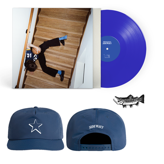 A blue vinyl record by Josh Gilligan, featuring an album cover of a person sprawled on stairs, a blue AS Colour Surf Caps outdoor snapback with a white star and "SIDEWAYS" text, and a small fish-shaped pin.